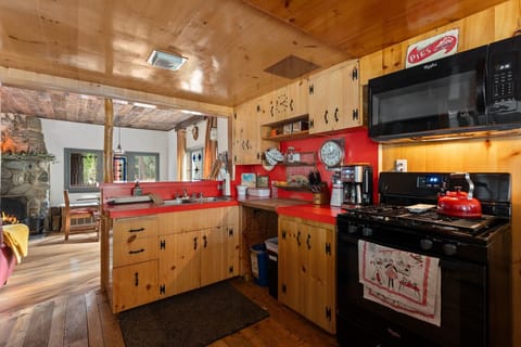 The open layout connects to a living area with a stone fireplace, creating a welcoming cabin atmosphere.