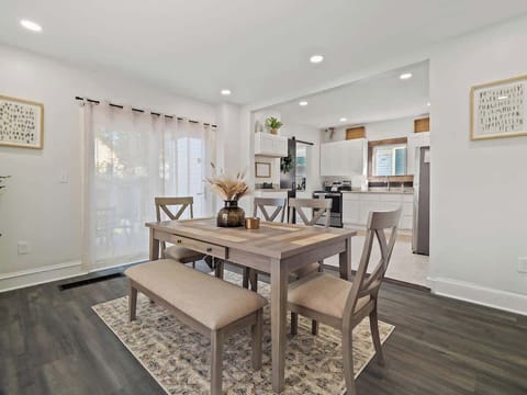 Light-filled dining area w/ table, bench & chairs set beside large windows