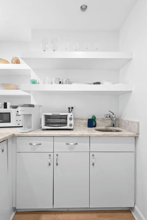 Kitchenette with a Toaster oven, microwave, mini fridge, Keurig coffee maker, glasses, plates, and cutlery.