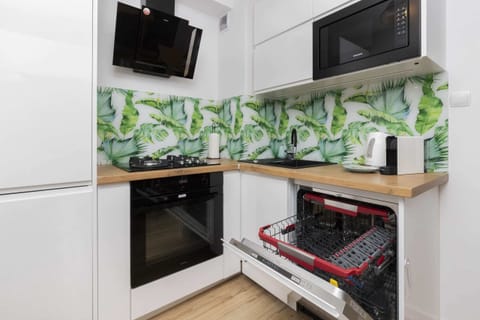A modern kitchen with a vibrant green leaf-patterned backsplash, a white microwave, and an electric oven.
