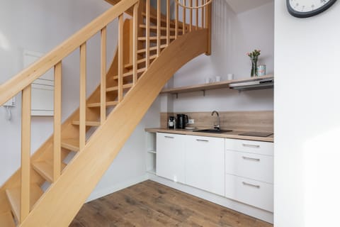 A kitchen area with white cabinets, wooden countertops, and a staircase in the corner.