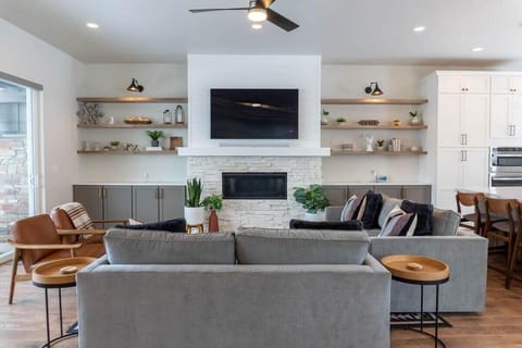 The living room is set up with everything you need for a relaxing space with an electrical fireplace, 65” smart TV, two sofas and two chairs, and well-placed decor creating a cozy home ambiance.