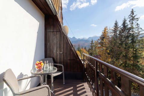 A charming balcony with a small table and chairs overlooking a forested mountain view.
