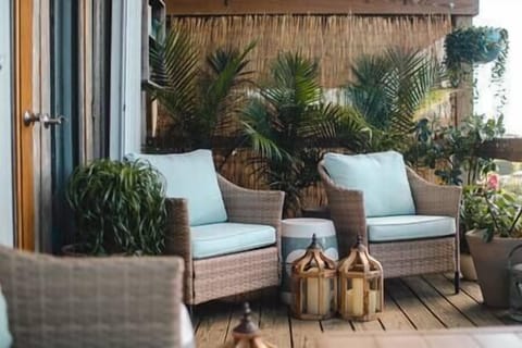 Porch features plants, candles, a bench seat and two chairs as well as a table 
