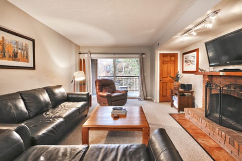 - Living room with modern seating and mountain views  
- Brick fireplace and flat screen TV for cozy nights  
- Open layout connects to dining and outdoor balcony