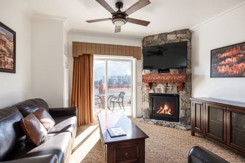 Relax after a day on the slopes in a warm living room with a stone fireplace, flat-screen TV, and direct access to your private balcony overlooking Canyons Village.
