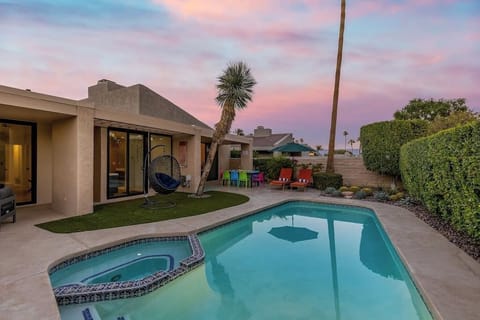 Twilight backyard with heated pool, spa, hang egg chair, and colorful patio dining — the reason guests book and keep coming back