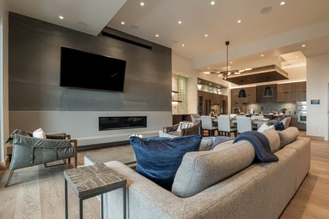 Large and open living room, kitchen, and dining area with sectional, gas fireplace, Smart TV, private deck access, dining room table, fully equipped kitchen, gas range, stone countertops, and island with seating