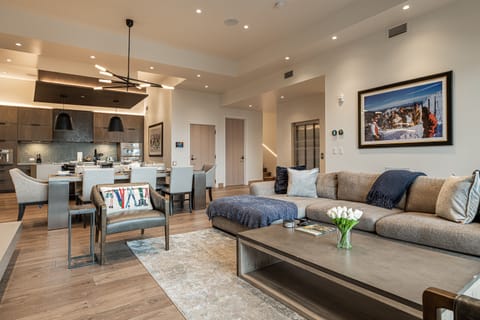 Large and open living room, kitchen, and dining area with sectional, gas fireplace, Smart TV, private deck access, dining room table, fully equipped kitchen, gas range, stone countertops, and island with seating