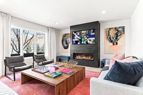     Modern family room with fireplace, vibrant art, and football broadcast.