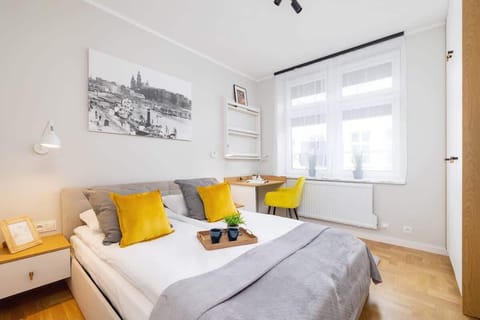 A bright bedroom with a double bed, yellow accent pillows, minimalist decor, and large windows, creating a cheerful and inviting sleeping space.
