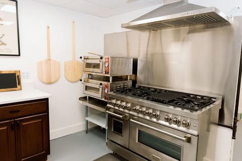 Commercial kitchen with pizza ovens, dual ovens, and prep space.