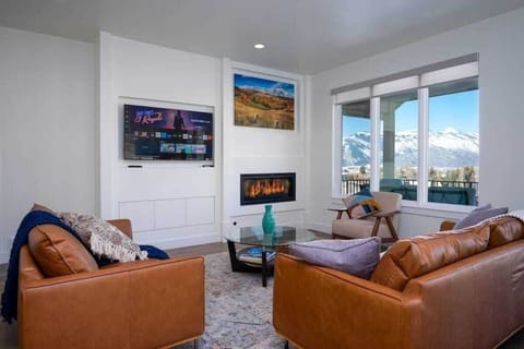 Experience the charm of Powder Ridge Escape's cozy living room, outfitted with plush seating, an expansive smart TV, and gas fireplace. Enjoy the large windows that frame the breathtaking mountain vistas.