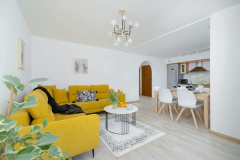 A bright and modern living room with a vibrant yellow sofa, a white coffee table, and contemporary decor creating a cozy atmosphere.