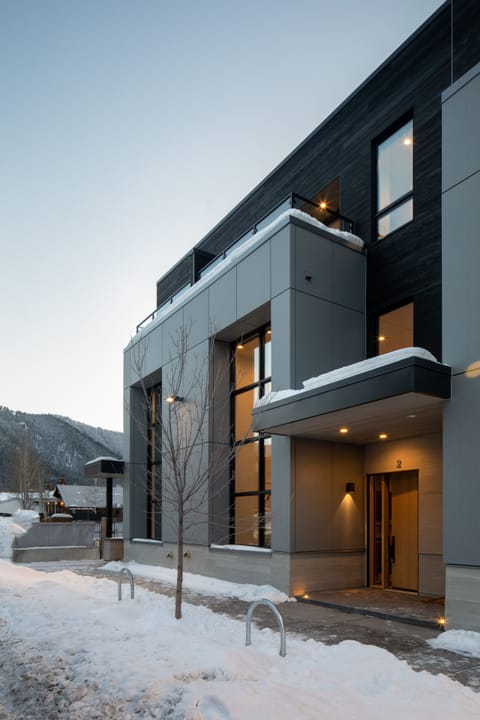 Step into your stylish mountain retreat where modern architecture meets alpine charm. The warm glow from your windows creates a welcoming beacon against the crisp winter landscape.