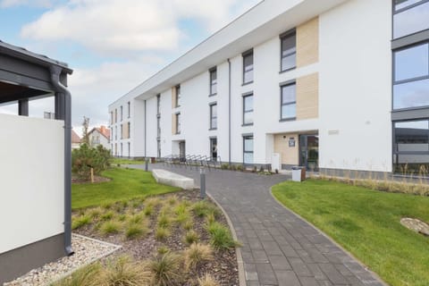 A view of the exterior of a modern apartment building with a clean, minimalist design and a landscaped walkway.
