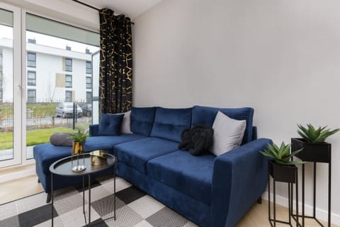 A stylish living room featuring a deep blue L-shaped sofa, a coffee table, and modern decor elements with a view of the garden outside.