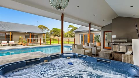 Solar heated swimming pool and hot tub spa beside a sundrenched deck and sheltered alfresco dining with gas mains BBQ, sun umbrella, and outdoor living area. 