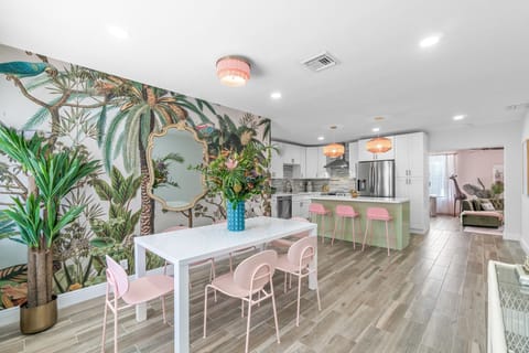 The dining room is outfitted with a modern white dining table, 6 whimsical mid-century palette pink dining chairs and unique Oahu fringe chandelier.