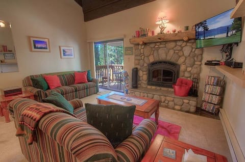 Living room with sofas, coffee table, fireplace, TV, shelves, media rack, sliding door, and balcony in view.