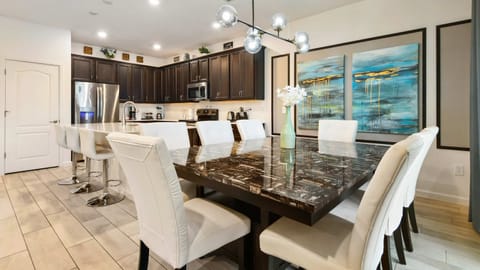 Elegant dining area with a sleek marble table, modern lighting, and a full kitchen.