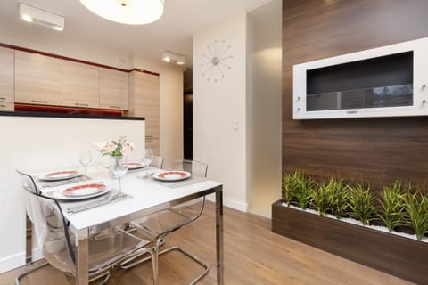 Elegant dining area features a modern table with chairs and a large mirror on the wall, creating a sense of depth in the room. The kitchen is visible in the background, blending seamlessly with the dining space.