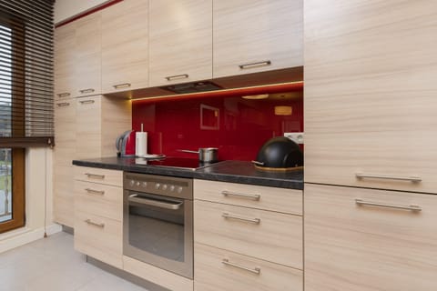 The kitchen has a vibrant red backsplash, sleek cabinets, and modern appliances. The space is well-equipped for cooking, offering both functionality and style.