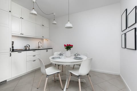 A clean, white kitchen with a dining area and pendant lights.
