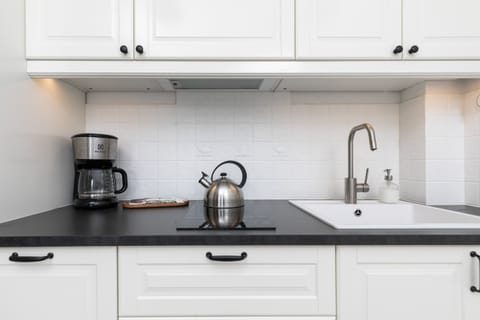 A kitchen counter with a coffee maker, kettle, and a backsplash of white tiles.
