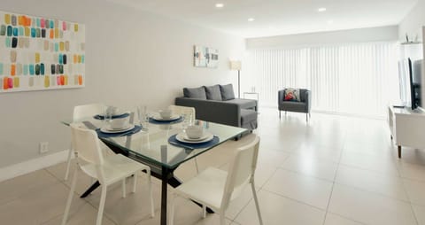 Bright dining and living area with sofa, chair, TV, and windows