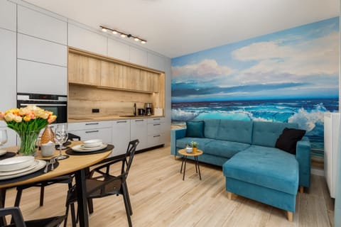 A bright living room with a turquoise couch, dining table, and scenic wall art.
