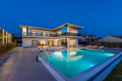 Illuminated pool with built-in waterfall on a spacious paved terrace with sun loungers and outdoor dining tables