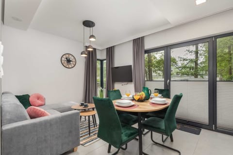 A stylish dining area with a round table, green chairs, and a large window providing natural light.

