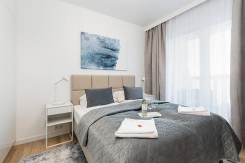 A cozy bedroom with a neatly made bed, soft gray bedding, and modern bedside tables.
