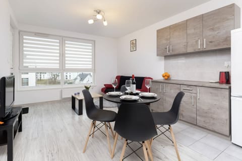 A modern and open living space featuring a red sofa, a sleek coffee table, and a dining table set for two, blending functionality and style.
