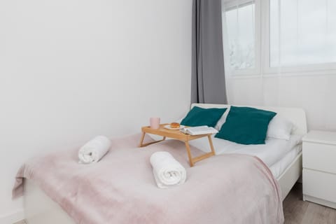 A bright bedroom with a comfortable bed, soft pink blanket, and neatly folded towels.

