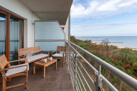 A balcony with wooden outdoor furniture, offering a comfortable seating area to enjoy the lush greenery and distant ocean views.