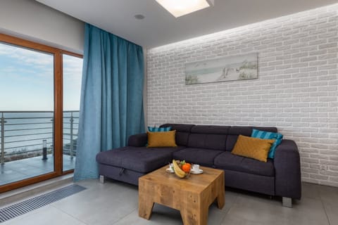 A cozy living room with a gray couch and blue curtains, featuring a wooden coffee table and a view of a balcony, letting in plenty of natural light.