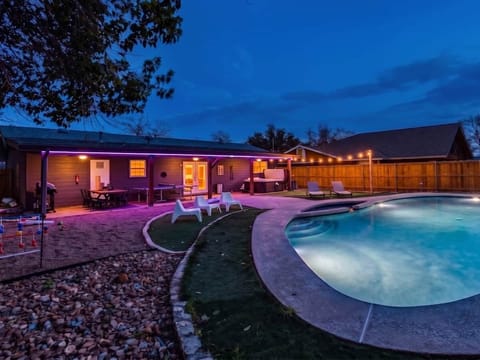 Stunning backyard oasis featuring a lighted pool, hot tub, and covered patio with purple LED accents. Includes an outdoor dining area, ping pong table, and cozy lounge spaces perfect for evening entertaining.