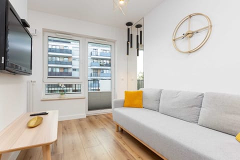 The centerpiece is a gray sofa with a yellow cushion. Nearby, the sleeping area features a bed covered with a navy blue throw, flanked by two bedside lamps.