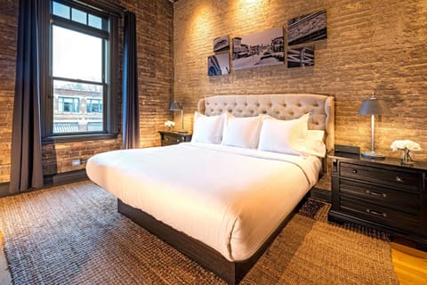 King bed, original brick, warm ambient lighting, and B&W photography on the wall. The bedroom earns its own moment.
