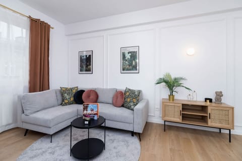 A bright and elegant living room with a modern gray sofa and wooden flooring.
