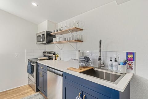 - Enjoy cooking in this sleek setup with stainless steel appliances and deep farmhouse sink
- Open shelves keep glassware and dishes within easy reach for every meal
- Navy blue cabinetry and white tile backsplash add bold modern charm