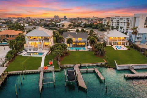 A sunset aerial showcases the waterfront setting, with a private pool, dock access, and the coastal skyline glowing in the distance.