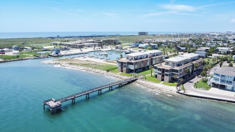 Stunning waterfront development with modern buildings, marina, and pier stretching into crystal-clear turquoise waters along this coastal community.