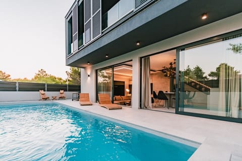 Patio with elegant private pool of 35 m2 and modern sun loungers with outdoor furniture with a preview of the interior living area in luxury vacation rental villa Noir in Vodice