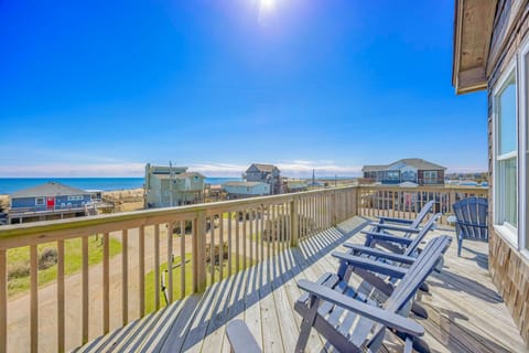 Coastal vacation rental deck with ocean views and surrounding beach houses under a bright blue sky.
