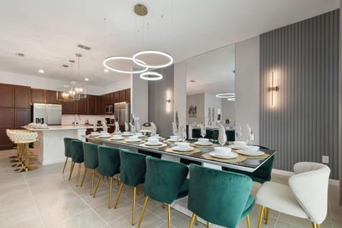 Stylish dining for twelve with velvet chairs, modern lighting, and open kitchen.