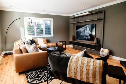 This cozy living room features a leather sofa, patterned armchair, and coffee table. Rustic touches like a horse photo, baskets, and plants pair with natural light and a tall floor lamp for a warm vibe.