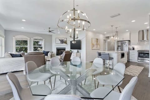 - Open concept layout connects dining, kitchen, and living room with ease - Statement chandelier over the glass dining table ties together the space elegantly - Crisp white cabinetry, wood flooring, and cozy seating create a warm, modern vibe